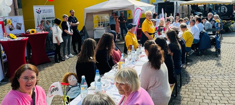 Ehrenamtliche sitzen an einer festlich gedeckten Tafel auf dem Wochenmarkt
