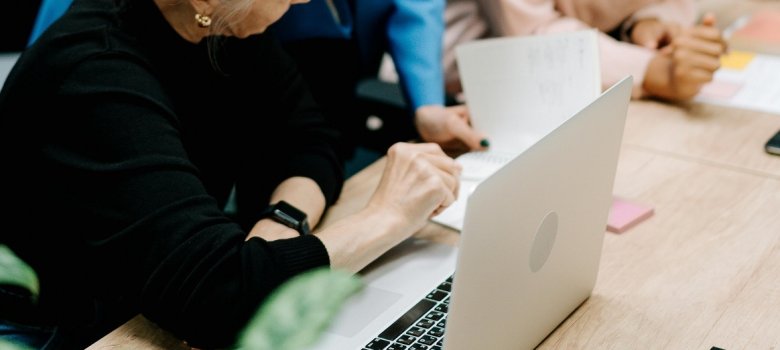 Menschen sitzen vor einem Tisch mit Laptop und reden