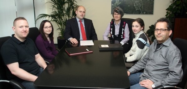 Das Bild zeigt sechs Personen, die an einem schwarzen Konferenztisch sitzen. Unter ihnen ist Bürgermeister Daniel Tybussek. Der Tisch ist groß und glänzend, darauf liegen Unterlagen und Mappen. Hinter dem Tisch stehen grüne Zimmerpflanzen. An der Wand hängt ein großes Bild. Die Personen blicken freundlich in die Kamera.