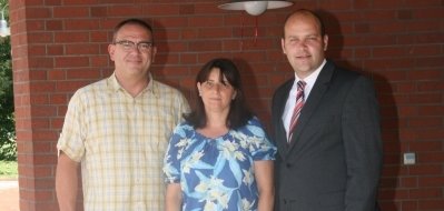 Das Bild zeigt drei Personen, die vor einem roten Backsteingebäude stehen. Über ihnen hängt ein gelbes Schild mit der Aufschrift "Städtische Kindertageseinrichtung Rathäuschen". Die Frau in der Mitte hält ein weißes Dokument in der Hand. Links neben ihr steht Bürgermeister Daniel Tybussek.