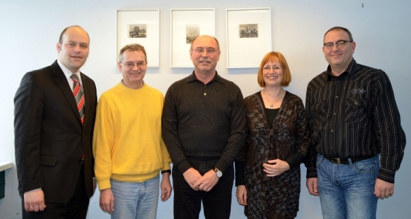 Fünf Personen stehen nebeneinander und lächeln in die Kamera. Im Hintergrund hängen drei Bilder an einer hellblauen Wand. Ganz links steht Bürgermeister Daniel Tybussek im Anzug mit roter Krawatte. Daneben stehen zwei Männer in einem gelben Pullover und einem schwarzen Pullover. Rechts neben ihnen steht eine Frau mit roten Haaren in einem schwarzen Outfit. Ganz rechts ist ein Mann mit Brille, Hemd und Jeans. Alle wirken freundlich und gut gelaunt.
