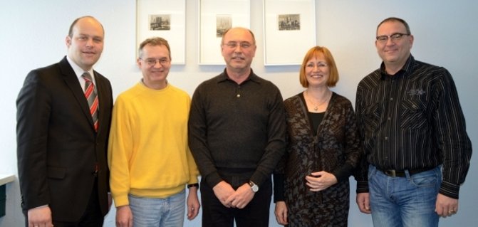 Fünf Personen stehen nebeneinander und lächeln in die Kamera. Im Hintergrund hängen drei Bilder an einer hellblauen Wand. Ganz links steht Bürgermeister Daniel Tybussek im Anzug mit roter Krawatte. Daneben stehen zwei Männer in einem gelben Pullover und einem schwarzen Pullover. Rechts neben ihnen steht eine Frau mit roten Haaren in einem schwarzen Outfit. Ganz rechts ist ein Mann mit Brille, Hemd und Jeans. Alle wirken freundlich und gut gelaunt.