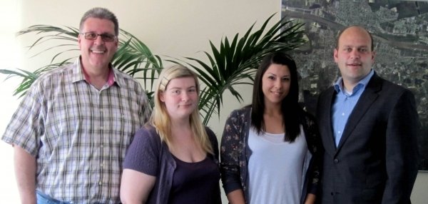 Auf dem Foto sind vier Personen in einem Raum zu sehen. Sie stehen nebeneinander und blicken freundlich in die Kamera. Links steht ein Mann mit Brille und kariertem Hemd, daneben eine junge Frau mit blonden Haaren im lila Oberteil. Rechts von ihr steht eine Frau mit dunklen Haaren. Sie trägt eine helle Bluse und eine dunkle Strickjacke. Ganz rechts steht Bürgermeister Daniel Tybussek im Anzug. Im Hintergrund sind grüne Pflanzen und ein großes Bild. Auf dem Bild sieht man die Stadtansicht von Mühlheim am Main.