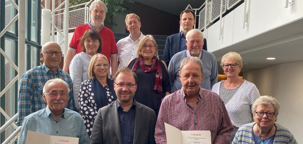 Mehrere Menschen stehen auf einer Treppe und lächeln. Zwei Männer halten eine Urkunde in den Händen. Sie wurden geehrt, weil sie sich um Gräber kümmern. Der Bürgermeister ist auch auf dem Bild. Die Gruppe gehört zu einem Verein aus Lämmerspiel.