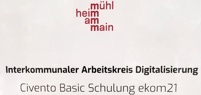 Das Bild zeigt ein Schild an einer Tür. Oben steht: Raum 15 - Benjamin Franklin. Das ist der Name und die Nummer des Raumes. Darunter ist ein rotes Logo mit den Worten: Mühlheim am Main. Weiter unten steht: Interkommunaler Arbeitskreis Digitalisierung. Das bedeutet: Menschen aus verschiedenen Städten arbeiten hier zusammen. Dann steht dort: Civento Basic Schulung ekom21. Das ist der Name einer Schulung. Ganz unten steht: 18. - 19. September 2024. Das sind die Tage, an denen die Schulung stattfindet. In dieser Schulung lernen Menschen, wie sie in ihren Städten Computerprogramme nutzen können. Die Stadt Mühlheim hat das Treffen organisiert. 