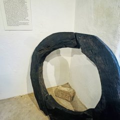 Das große schwarze Holzstück steht an einer weißen Wand. Daneben ist eine Tafel mit Informationen. Auf dem Boden liegt ein Stein mit der Zahl 1643.