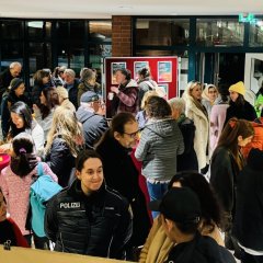 Ein Raum voller Menschen. Sie reden miteinander und informieren sich über das Thema Gewalt gegen Frauen, Eine Polizistin ist auch dabei.