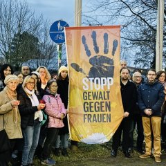 Eine Gruppe Menschen steht draußen vor einer Fahne. Auf der Fahne steht "Stopp Gewalt gegen Frauen". Bürgermeister Dr. Alexander Krey ist dabei. Einige Menschen halten Kerzen in der Hand.