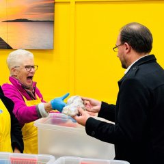 Eine ältere Frau mit Brille und pinker Jacke empfängt von Bürgermeister Dr. Alexander Krey einen Christstollen. Sie trägt blaue Handschuhe und eine gelbe Schürze. Beide lächeln.
